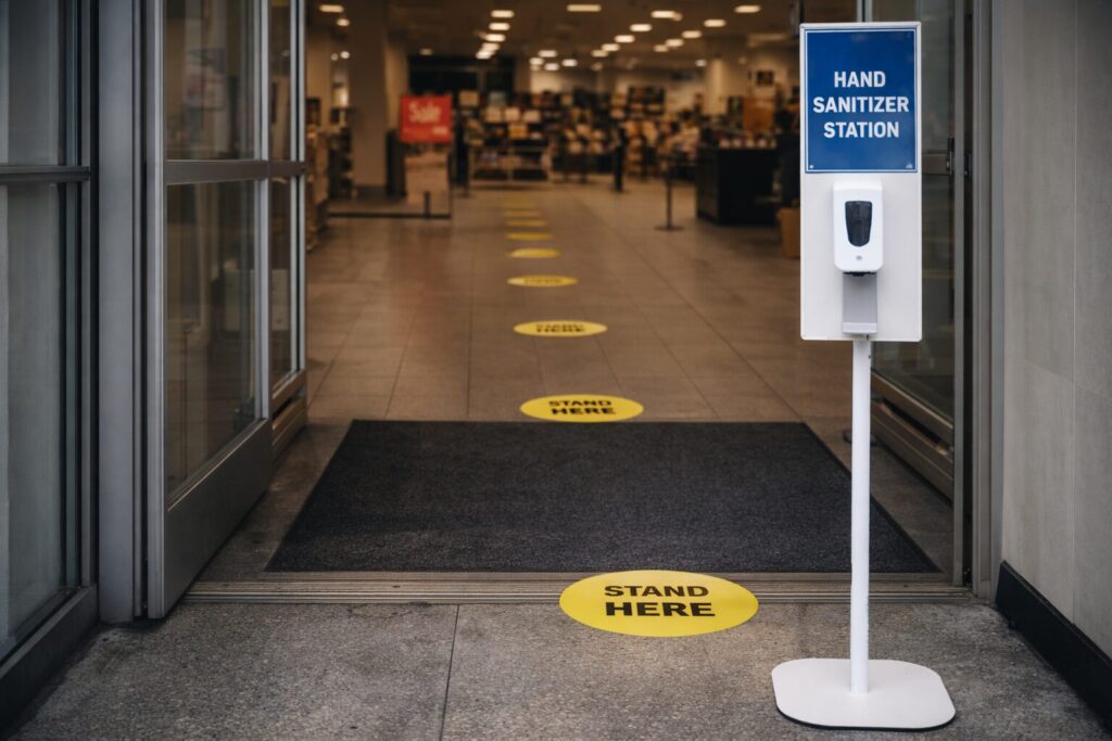 Empty retail entrance with spaced floor markers and a hand-sanitizer station, emphasizing that rules only matter when they’re enforced.